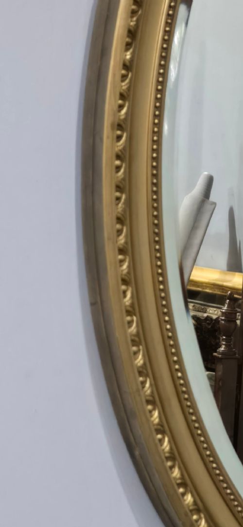 An antique oval wall mirror featuring a gilded frame decorated with beaded and egg-and-dart moulded trim. View IV