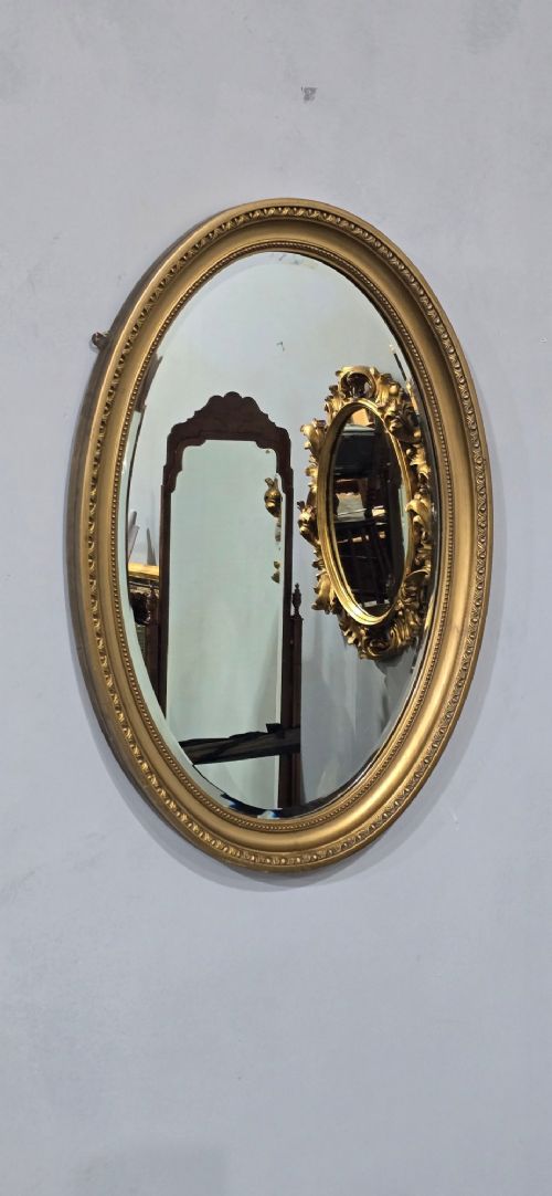 An antique oval wall mirror featuring a gilded frame decorated with beaded and egg-and-dart moulded trim. View VIII
