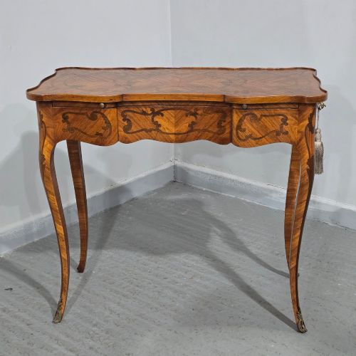 fig 1. A small French Louis XV style writing table crafted from warm brown wood with scrolling marquetry, a serpentine edge, and slim cabriole legs.