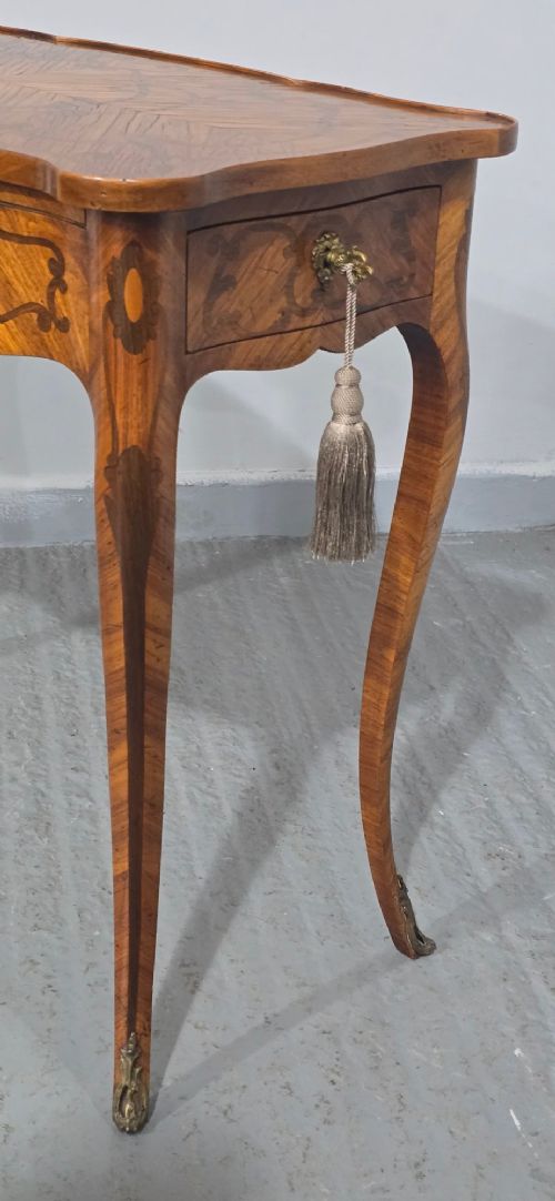 A small French Louis XV style writing table crafted from warm brown wood with scrolling marquetry, a serpentine edge, and slim cabriole legs. View IV