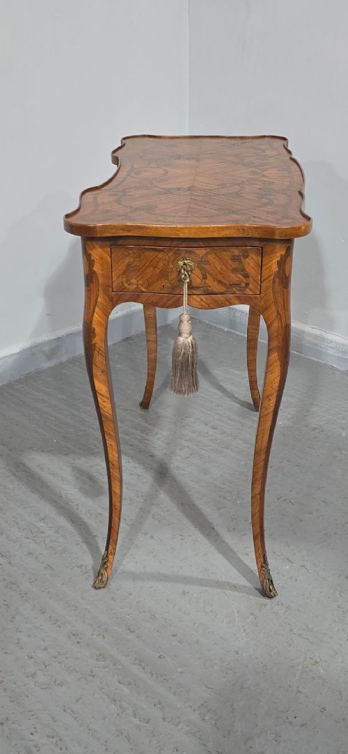 A small French Louis XV style writing table crafted from warm brown wood with scrolling marquetry, a serpentine edge, and slim cabriole legs. View X
