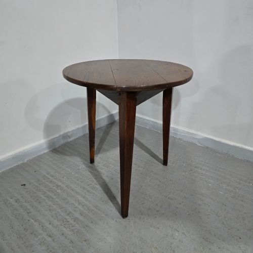 fig 1. A dark brown Georgian oak cricket table featuring a circular planked top supported by three splayed tapered legs.
