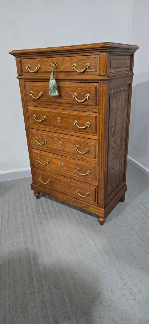 A tall French oak chest of drawers featuring six stacked drawers, brass swing handles, fluted side pilasters, and turned wooden feet. View VII