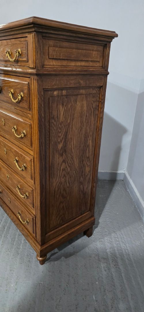 A tall French oak chest of drawers featuring six stacked drawers, brass swing handles, fluted side pilasters, and turned wooden feet. View VIII