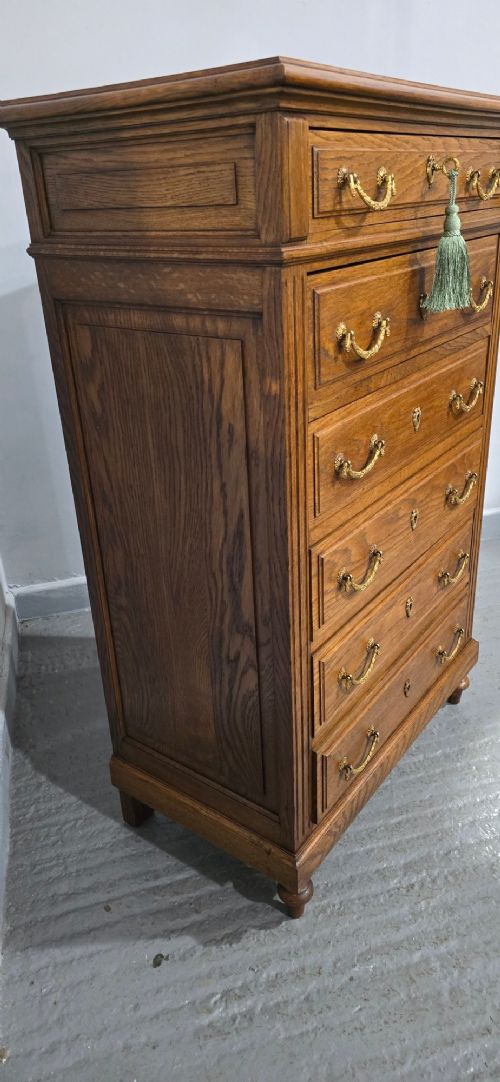 A tall French oak chest of drawers featuring six stacked drawers, brass swing handles, fluted side pilasters, and turned wooden feet. View IX