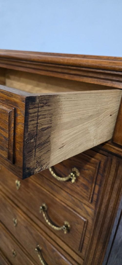 A tall French oak chest of drawers featuring six stacked drawers, brass swing handles, fluted side pilasters, and turned wooden feet. View XII