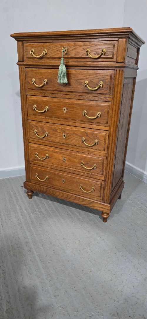 A tall French oak chest of drawers featuring six stacked drawers, brass swing handles, fluted side pilasters, and turned wooden feet. View XIV