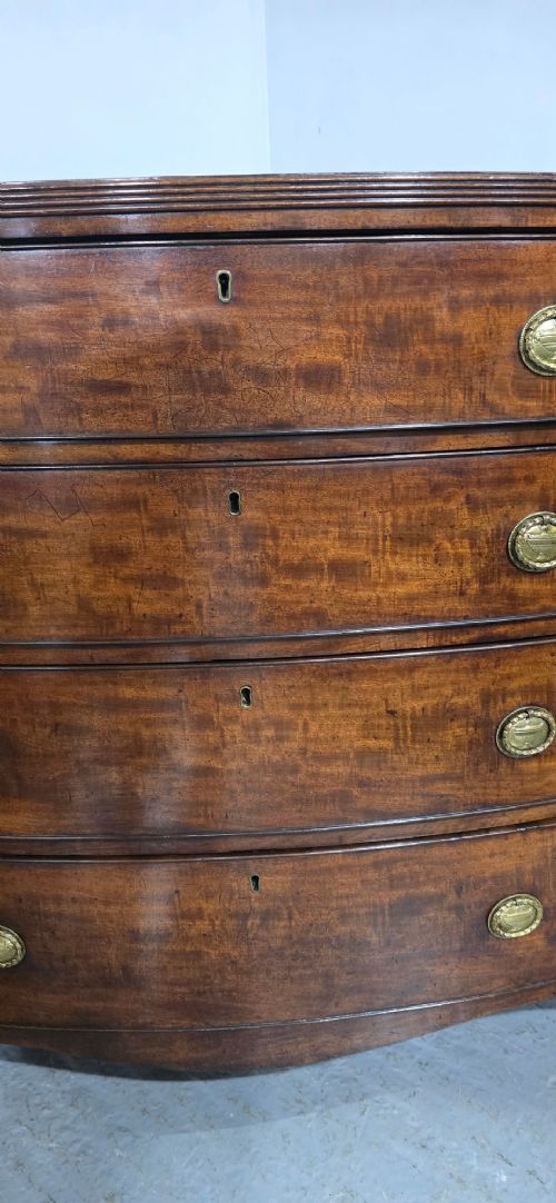 A Georgian mahogany bowfront chest of drawers featuring four graduated drawers with oval brass handles and splayed feet. View IV