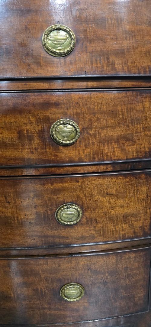 A Georgian mahogany bowfront chest of drawers featuring four graduated drawers with oval brass handles and splayed feet. View V