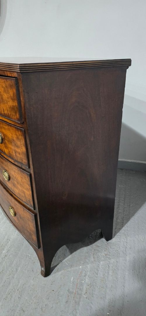 A Georgian mahogany bowfront chest of drawers featuring four graduated drawers with oval brass handles and splayed feet. View VII