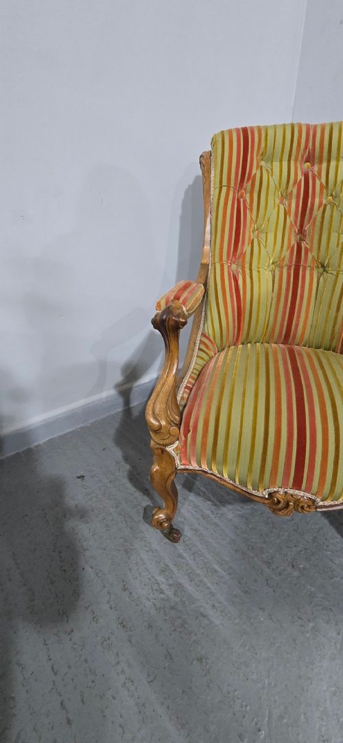 A Regency style rosewood library armchair with button-tufted striped upholstery, carved scroll arms, cabriole legs, and brass castors. View V