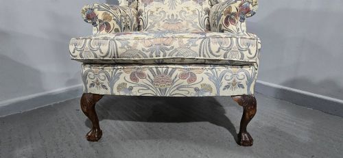 fig 1. A high-backed wingback armchair upholstered in a botanical pattern with dark carved cabriole legs and ball-and-claw feet.