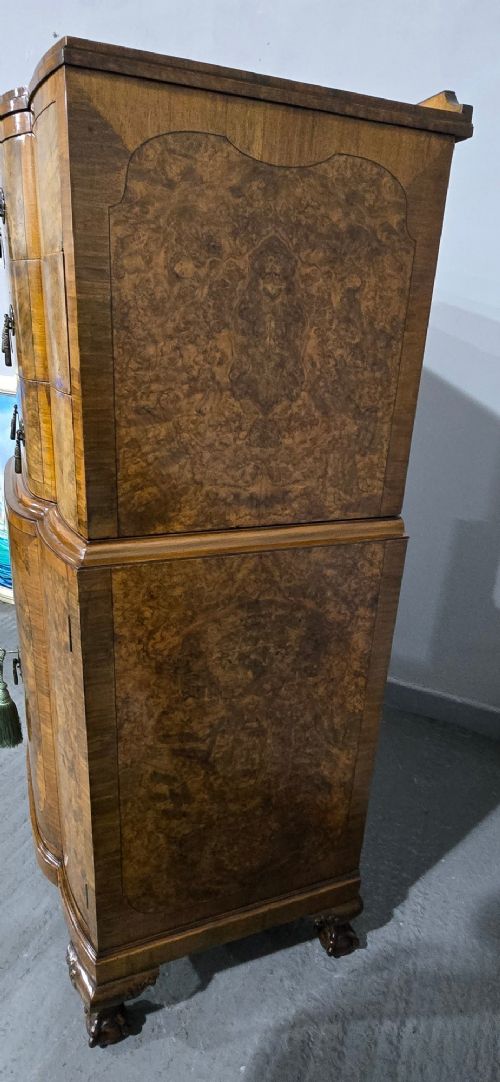 An antique burr walnut linen press featuring an upper drawer section and lower double-door cupboard supported by carved ball and claw feet. View V
