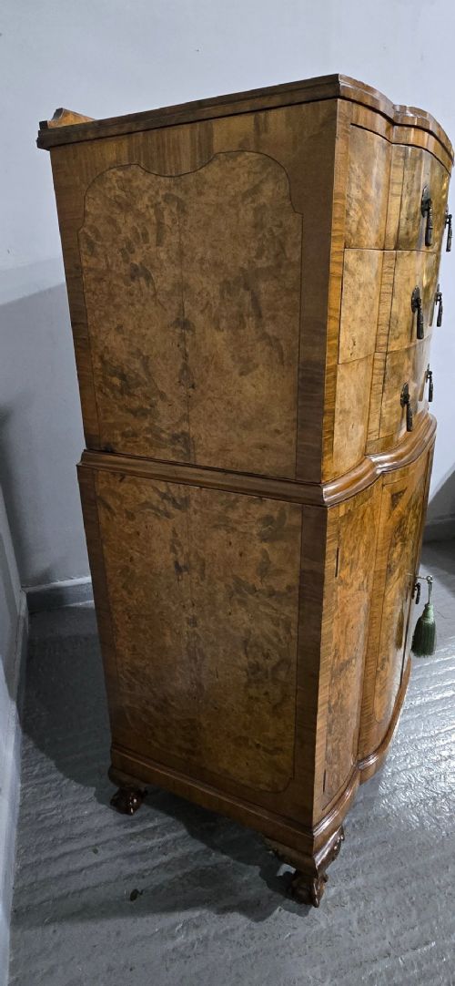 An antique burr walnut linen press featuring an upper drawer section and lower double-door cupboard supported by carved ball and claw feet. View VI