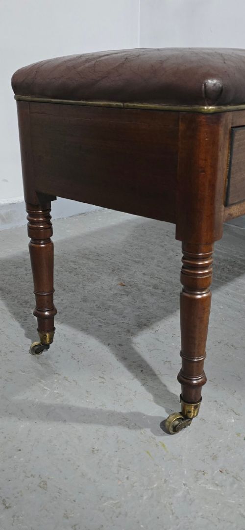 A Regency period mahogany duet stool with a brown leather upholstered top, two front frieze drawers with round brass knobs, and four turned legs on brass castors. View VI
