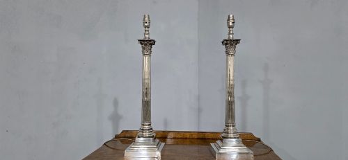 fig 1. A pair of silver-plated table lamps styled as fluted Corinthian columns on stepped square bases, fitted with white pleated shades with beaded trim.