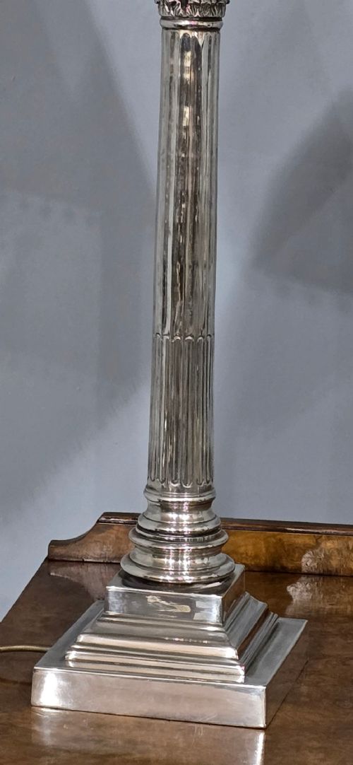 A pair of silver-plated table lamps styled as fluted Corinthian columns on stepped square bases, fitted with white pleated shades with beaded trim. View IX