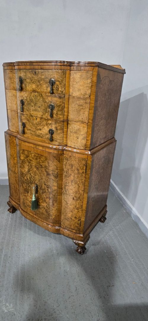 A two-section burr walnut linen press featuring a breakfront profile, upper drawers with drop handles, lower cupboard doors, and carved cabriole legs. View XV