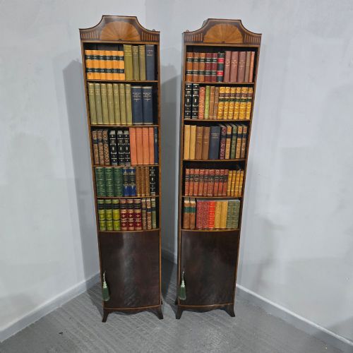 fig 1. A pair of tall, narrow mahogany open bookcases featuring inlaid fan motifs at the arched top, adjustable shelves filled with books, and lower cupboard doors.