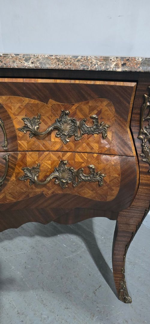 A French Louis XV style bombe commode featuring detailed floral marquetry inlay, bronze mounts, curved legs, and a brown marble top. View V