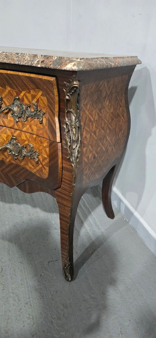 A French Louis XV style bombe commode featuring detailed floral marquetry inlay, bronze mounts, curved legs, and a brown marble top. View VI