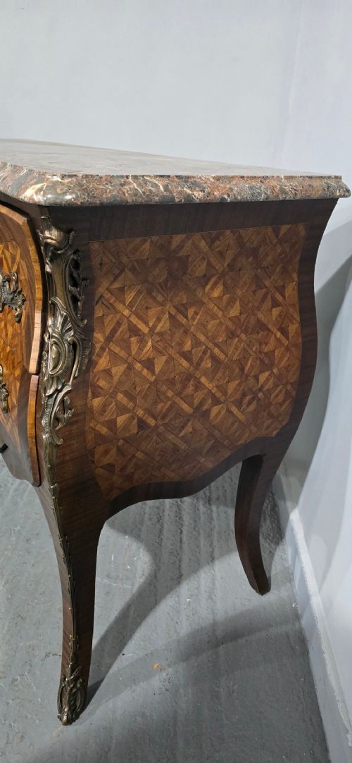 A French Louis XV style bombe commode featuring detailed floral marquetry inlay, bronze mounts, curved legs, and a brown marble top. View VII