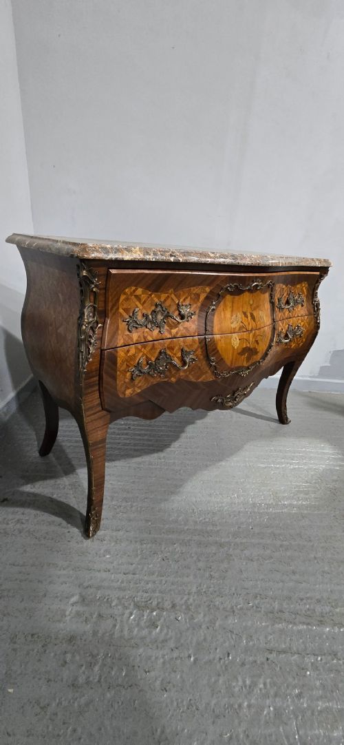 A French Louis XV style bombe commode featuring detailed floral marquetry inlay, bronze mounts, curved legs, and a brown marble top. View XII