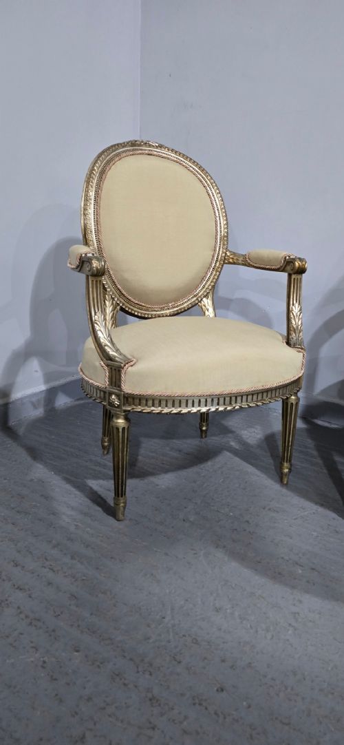 A pair of French Louis XVI style open armchairs featuring carved giltwood frames with oval medallion backs, fluted legs, and neutral cream upholstery. View V