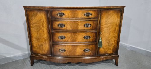 fig 1. A bow-front mahogany sideboard featuring four central drawers flanked by two side cupboard doors with oval brass handles and flame mahogany grain patterns.