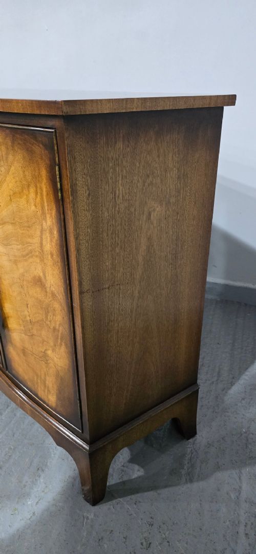 A bow-front mahogany sideboard featuring four central drawers flanked by two side cupboard doors with oval brass handles and flame mahogany grain patterns. View VII