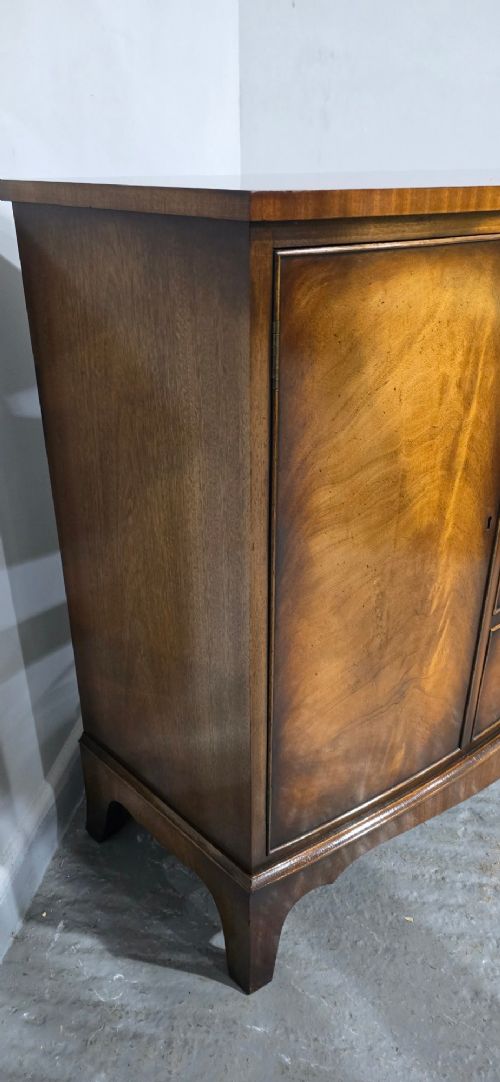 A bow-front mahogany sideboard featuring four central drawers flanked by two side cupboard doors with oval brass handles and flame mahogany grain patterns. View VIII