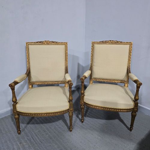 fig 1. A pair of French Neoclassical giltwood open armchairs upholstered in neutral fabric with fluted tapered legs and carved square backs.