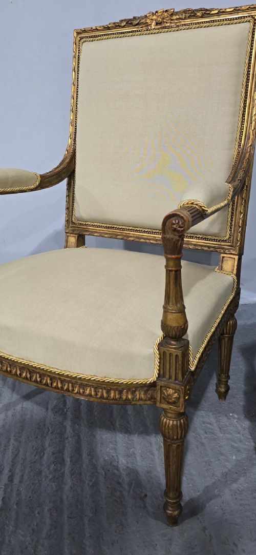 A pair of French Neoclassical giltwood open armchairs upholstered in neutral fabric with fluted tapered legs and carved square backs. View V