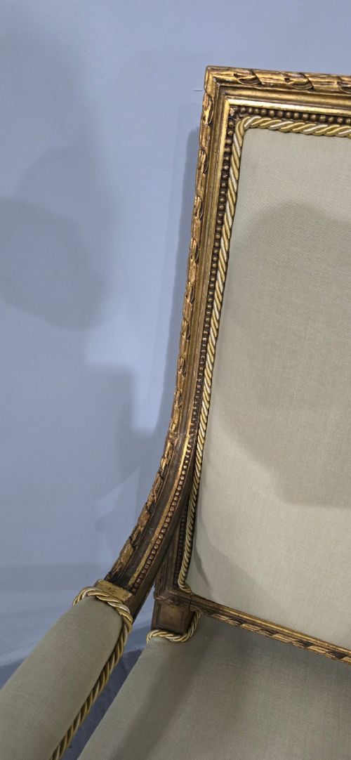 A pair of French Neoclassical giltwood open armchairs upholstered in neutral fabric with fluted tapered legs and carved square backs. View VII