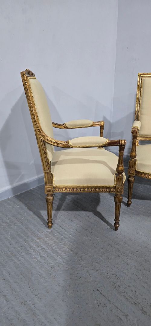A pair of French Neoclassical giltwood open armchairs upholstered in neutral fabric with fluted tapered legs and carved square backs. View IX