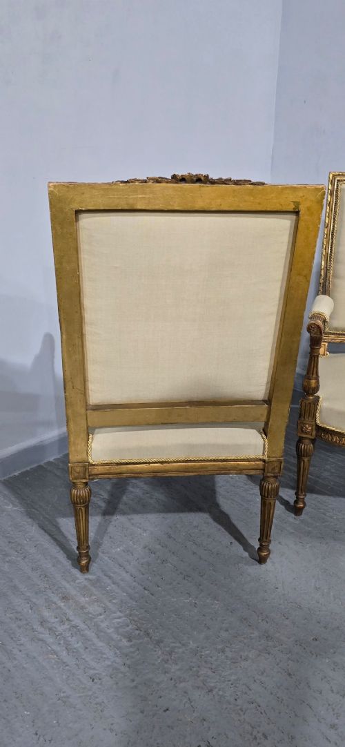 A pair of French Neoclassical giltwood open armchairs upholstered in neutral fabric with fluted tapered legs and carved square backs. View X