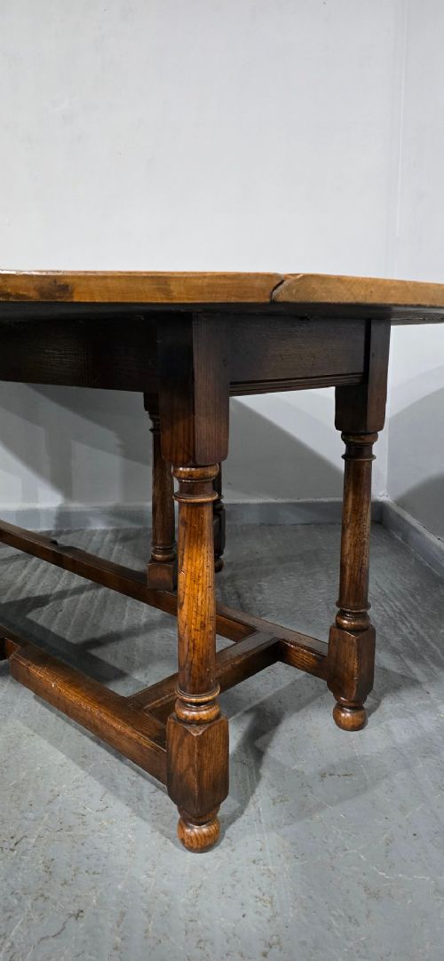 A large oval solid oak wake table featuring drop-leaf sides, turned legs, and square stretchers. View VIII