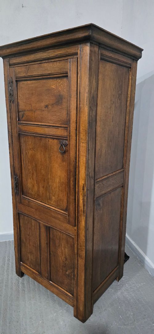 A tall, narrow antique dark oak food cupboard featuring panelled doors, hand-forged iron hinges, a metal ring drop handle, and a top moulded cornice. View V