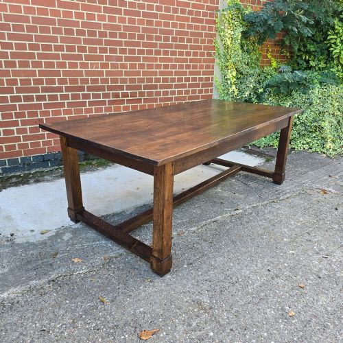 fig 1. A solid warm brown French oak refectory dining table featuring a rectangular plank top, square legs, and an H-stretcher base.