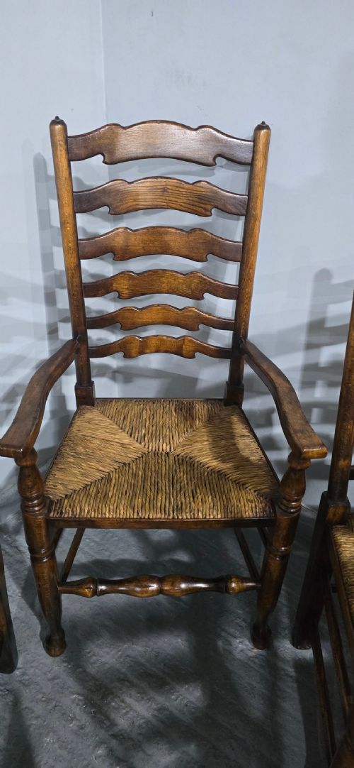 A set of twelve dark oak ladder back dining chairs featuring woven rush seats, shaped horizontal back slats, and turned front legs. View X