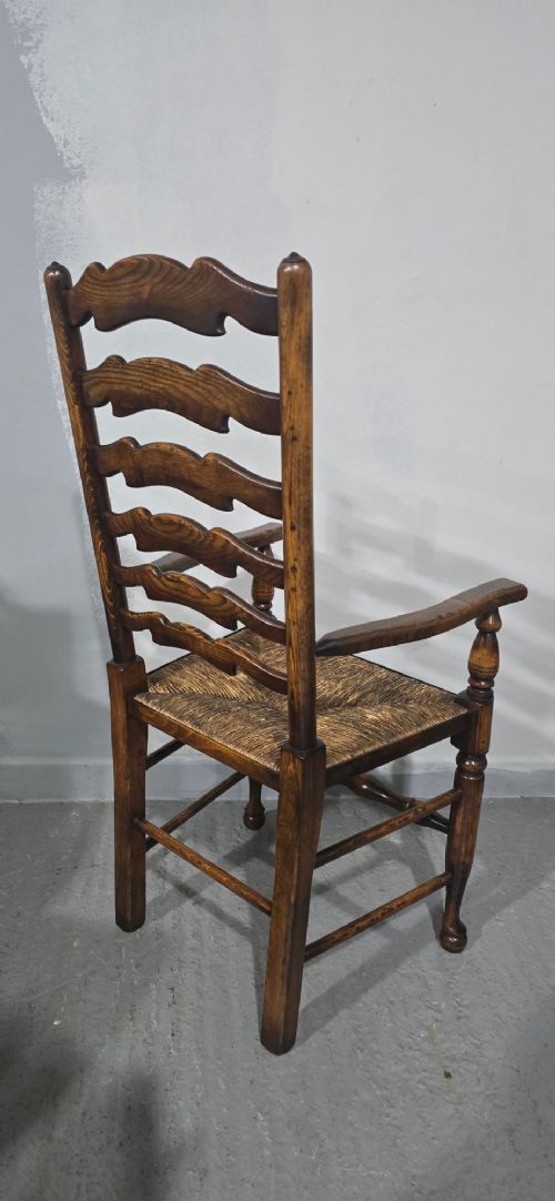 A set of twelve dark oak ladder back dining chairs featuring woven rush seats, shaped horizontal back slats, and turned front legs. View XII