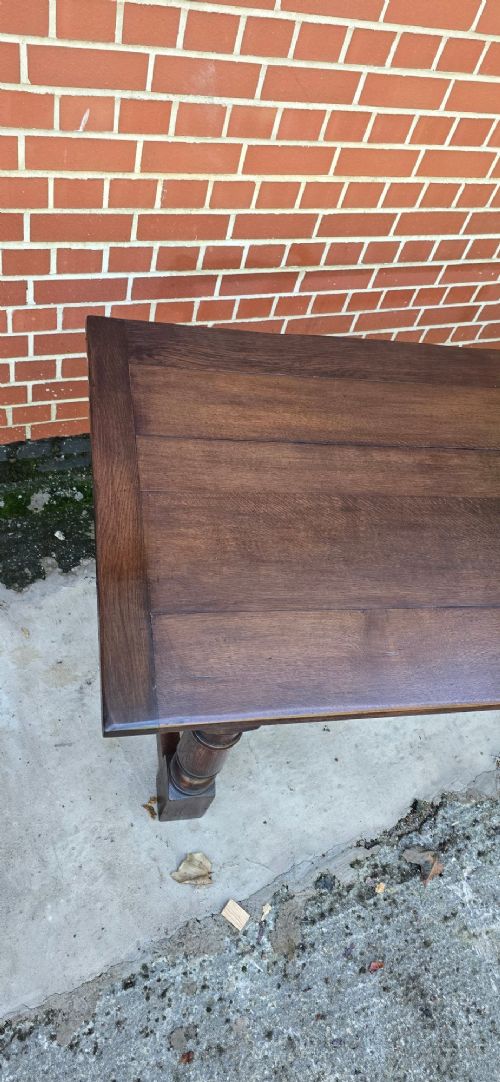 A solid dark oak refectory dining table with a plank top, stout turned legs, and an H-stretcher base. View VI
