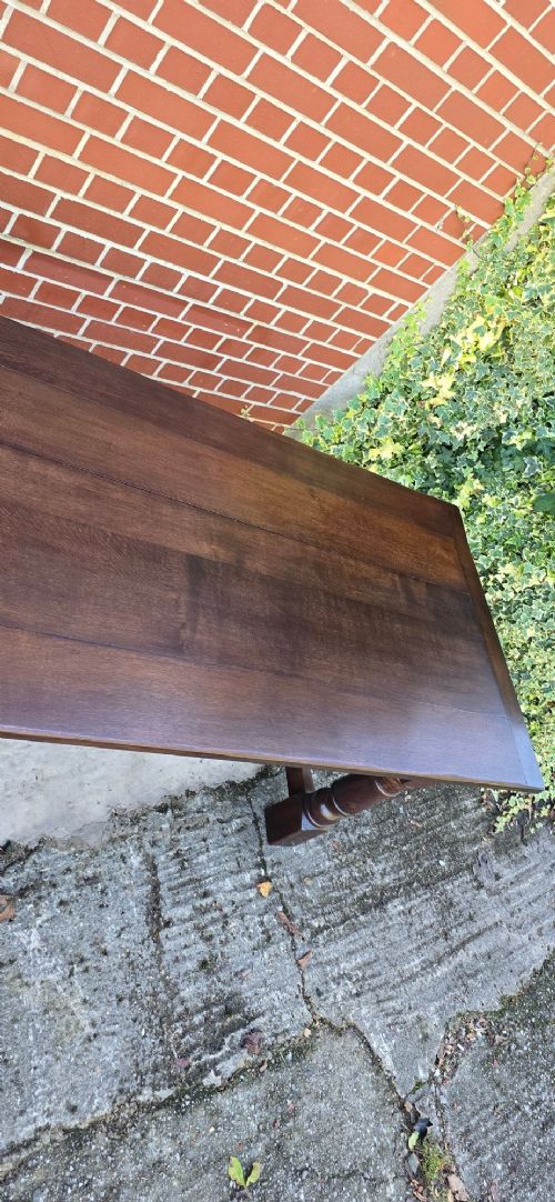 A solid dark oak refectory dining table with a plank top, stout turned legs, and an H-stretcher base. View VII