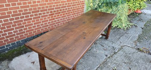 fig 1. A long solid French oak refectory dining table featuring a plank top and straight legs connected by a low stretcher.