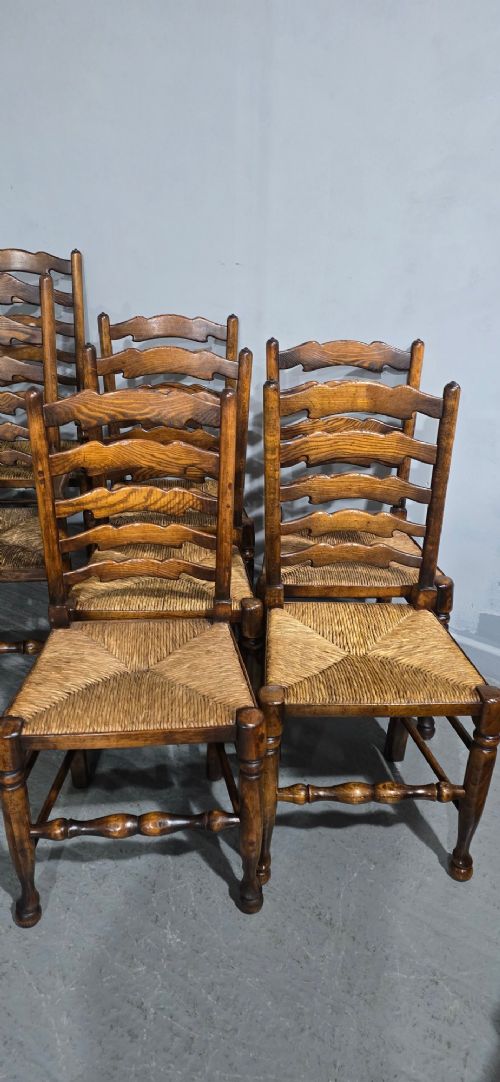 A set of twelve oak dining chairs featuring shaped ladder back slats, natural rush seats, and turned front legs. View V