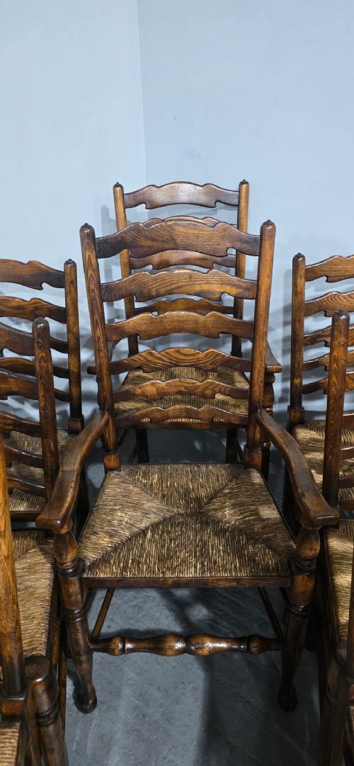 A set of twelve oak dining chairs featuring shaped ladder back slats, natural rush seats, and turned front legs. View VI
