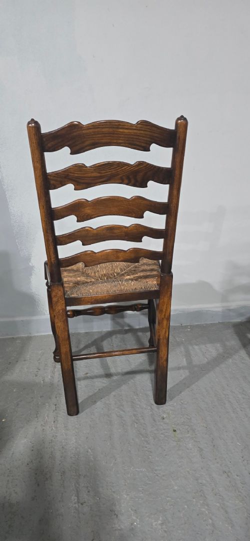 A set of twelve oak dining chairs featuring shaped ladder back slats, natural rush seats, and turned front legs. View X