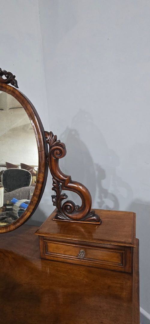 A Victorian mahogany dressing table featuring a central oval swivelling mirror, carved scroll supports, small upper trinket drawers, and twin drawer pedestals flanking a central cupboard. View V