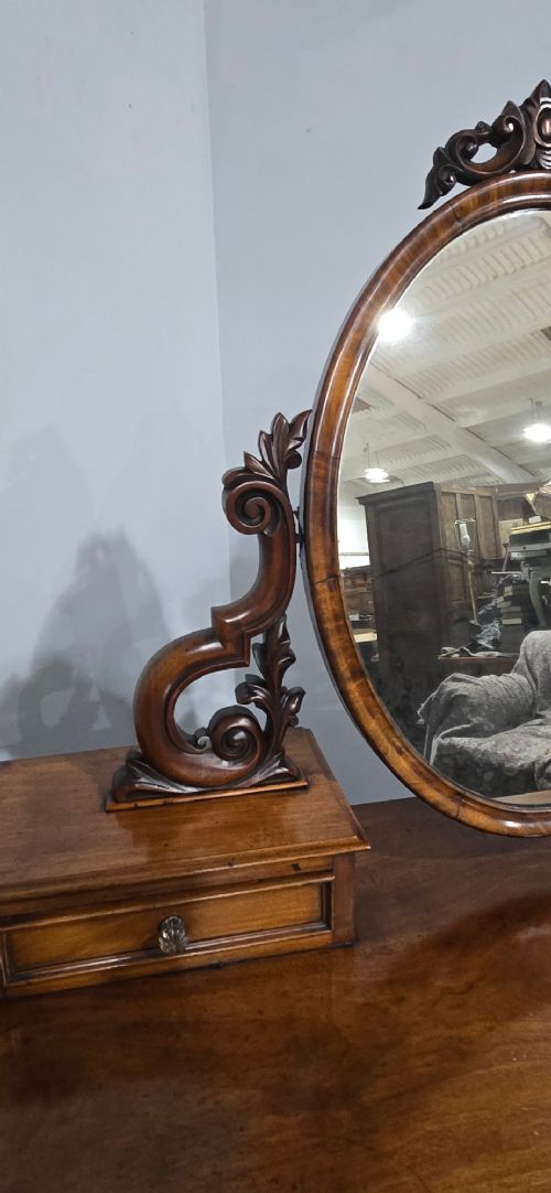 A Victorian mahogany dressing table featuring a central oval swivelling mirror, carved scroll supports, small upper trinket drawers, and twin drawer pedestals flanking a central cupboard. View VI