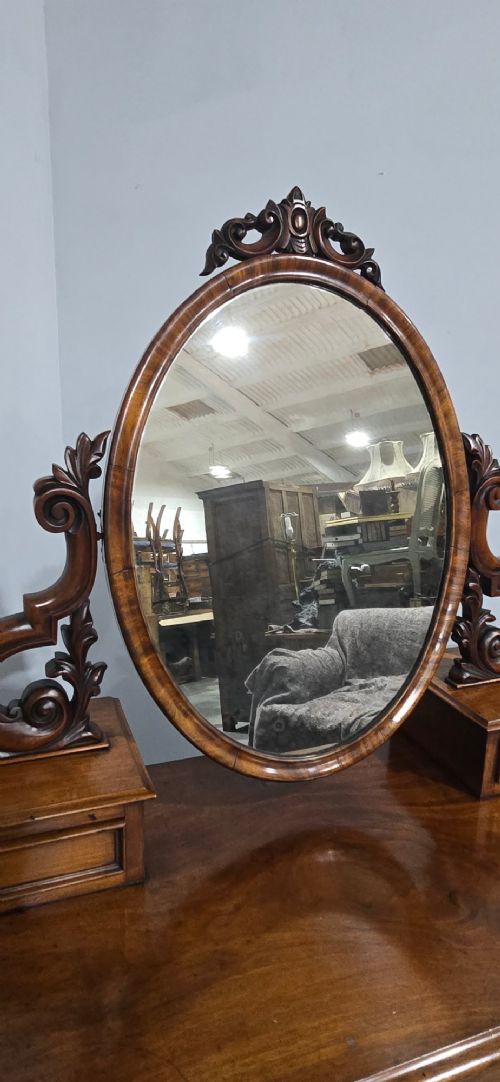 A Victorian mahogany dressing table featuring a central oval swivelling mirror, carved scroll supports, small upper trinket drawers, and twin drawer pedestals flanking a central cupboard. View VII